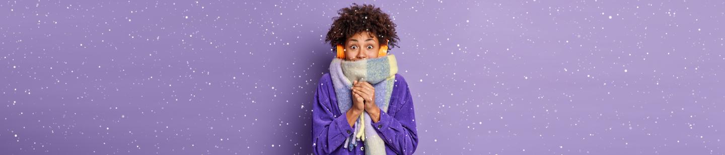 A woman in a winter scarf and headphones while snowflakes fall around her
