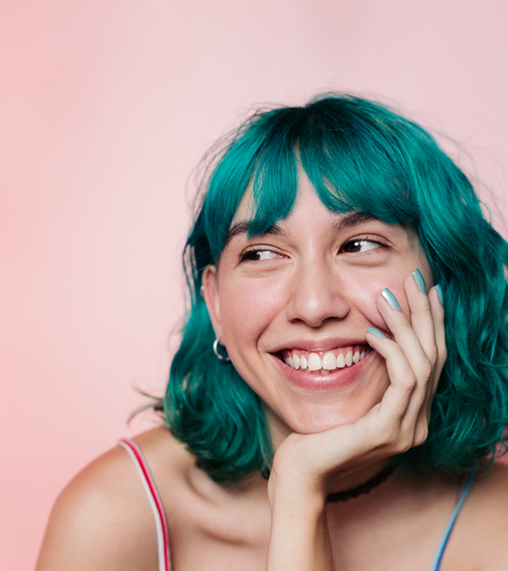 woman with blue hair and pink background looking to the left