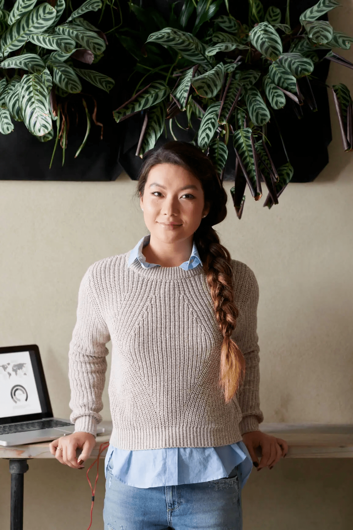 woman leaning on desk smiling with latop behind her