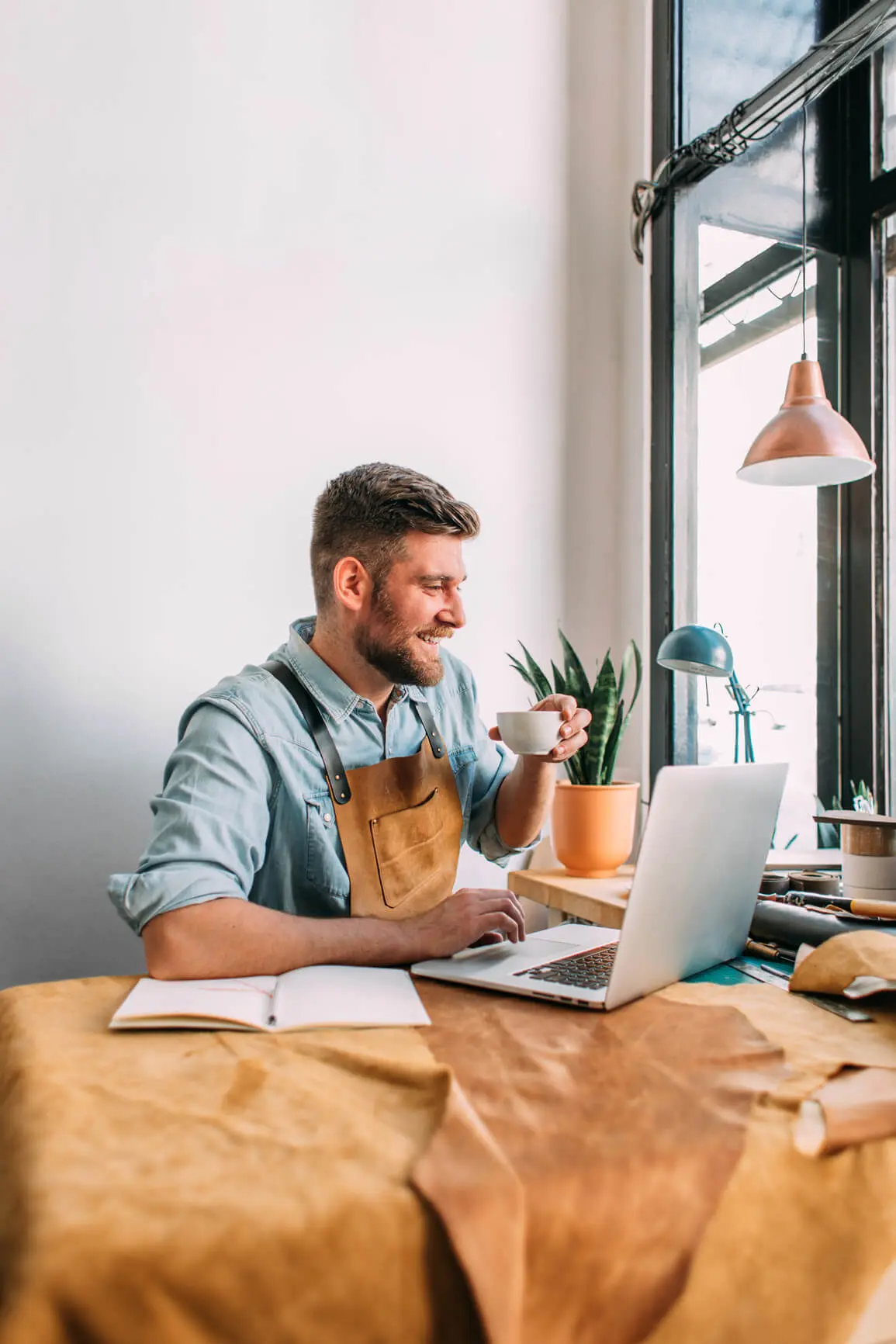 Man looking at laptop smiling while sipping coffee