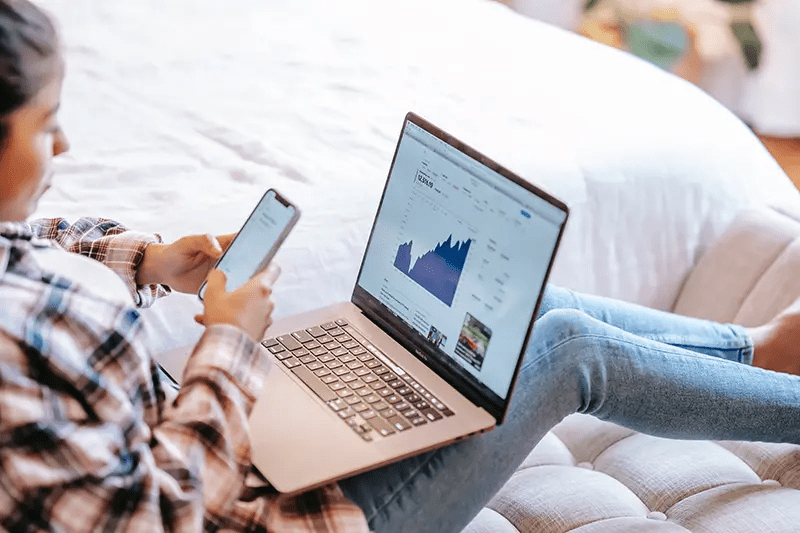 woman looking at phone with laptop