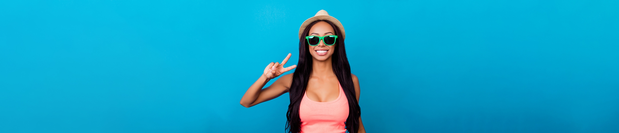 A woman in a pink shirt and green sunglasses, making the peace sign in front of a gradient blue background.