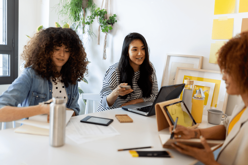 Women discussing at table with notepads and devices